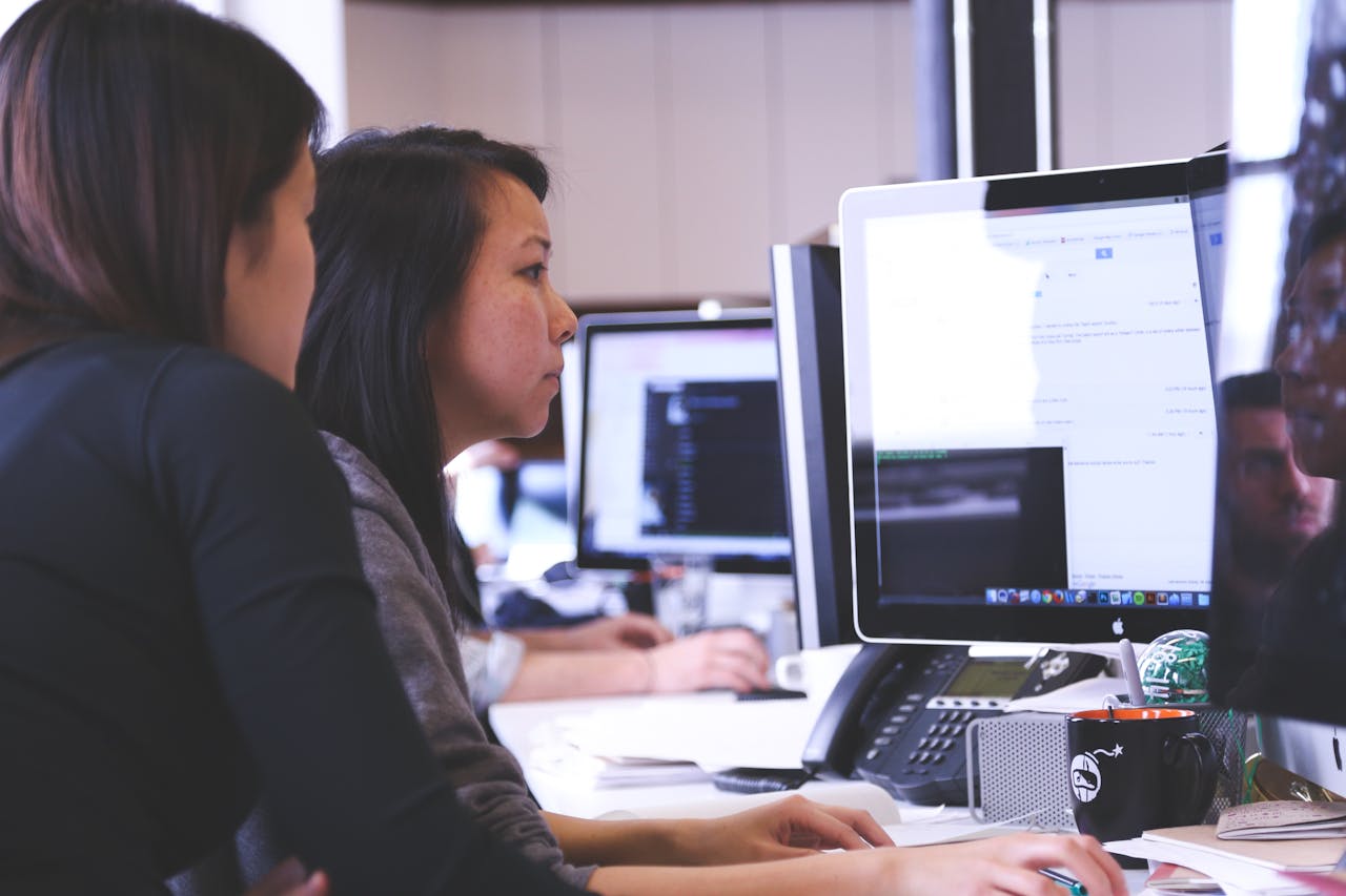 team-01 Two women working together on code at a computer in a modern office setting.